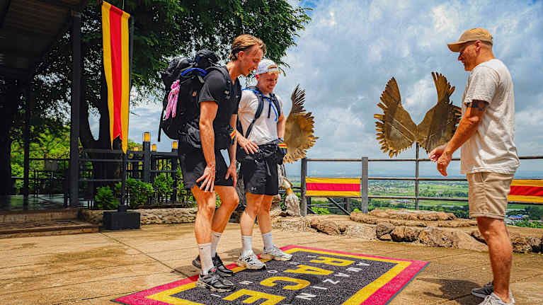 Ilmari Nurminen ja Aapo Hettula, shortseissa ja t-paidoissa, selässä isot reput, seisovat Amazin Race Suomi maton päällä. Edessä Heikki Paasonen.