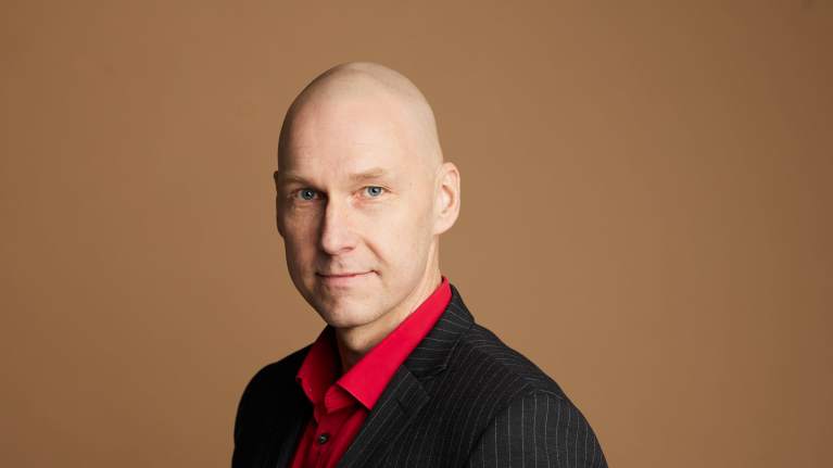 Näyttelijäliiton puheenjohtaja Antti Timonen punainen paita ja liituraitatakki yllään.