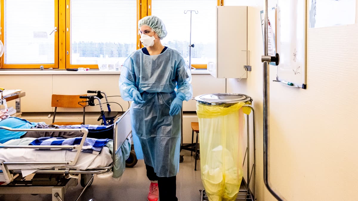 Suojavarusteisiin pukeutunut lähihoitaja Janina Kinnunen koronapotilaan kanssa.