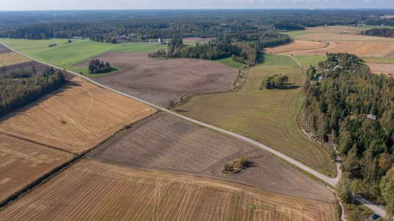 Flygfoto över vidsträckta jordbruksmarker med skördade åkrar och omgivande skog i ett lugnt landskap.