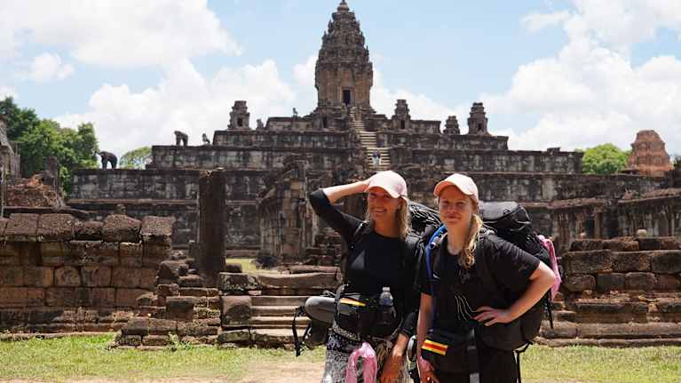 Maria Guzenina ja Vilma Vahamaa seisovat historiallisen temppelialueen edessä isot reput selässä.