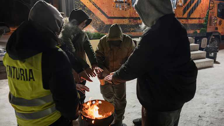 Ihmiset lämmittävät käsiään ulkonuotion äärellä.