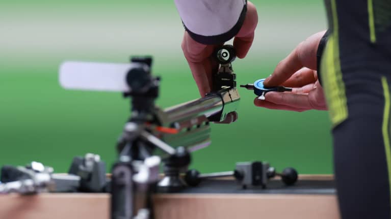 Urheilija laittaa asettaan valmiiksi Tokion olympialaisissa 50 metrin pienoiskiväärin moniasentokilpailussa.