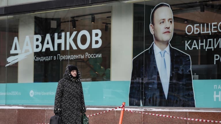 Talvivaatteisiin pukeutunut nainen kulkee kadulla ja kantaa kahta laukkua ohittaen Vladislav Davankovin kuvan rakennuksen näyteikkunassa. Ikkunassa on suurin kyrillisin kirjaimin teksti: Davankov. Venäjän presidenttiehdokas.