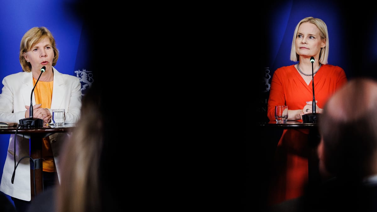 Swedish People's Party leader Anna Maja Henriksson on the left, in a white jacket against a blue background. A black space in the middle, and then Finns Party leader Riikka Purra, in a red top against a blue background. 
