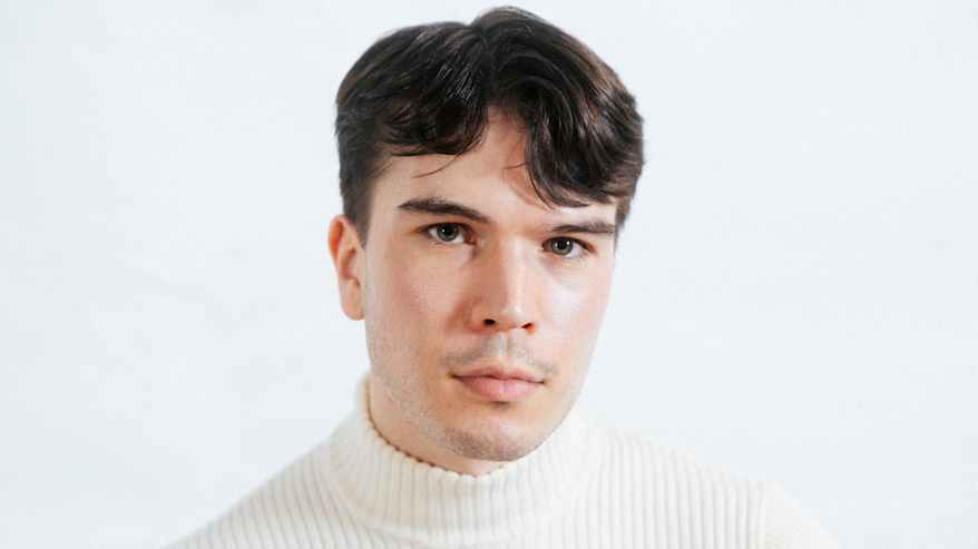 A person wearing a light sweater against a white background.