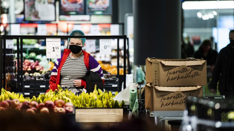 En kvinna står och tittar på prislappen på bananer i en större matbutiks frukt och grönt-avdelning.