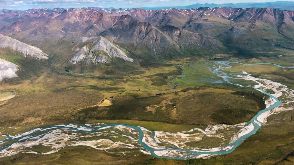 Alaskan arktisen luonnonsuojelualueen maisemaa kirkkaan sininen joki ja taustalla vuorenhuippuja