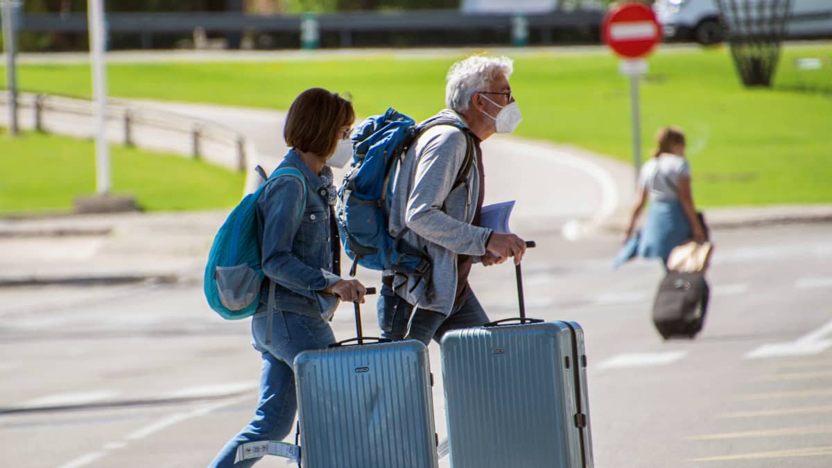 Maskipäinen pariskunta kuljettaa matkalaukkuja Mallorcan lentokentällä