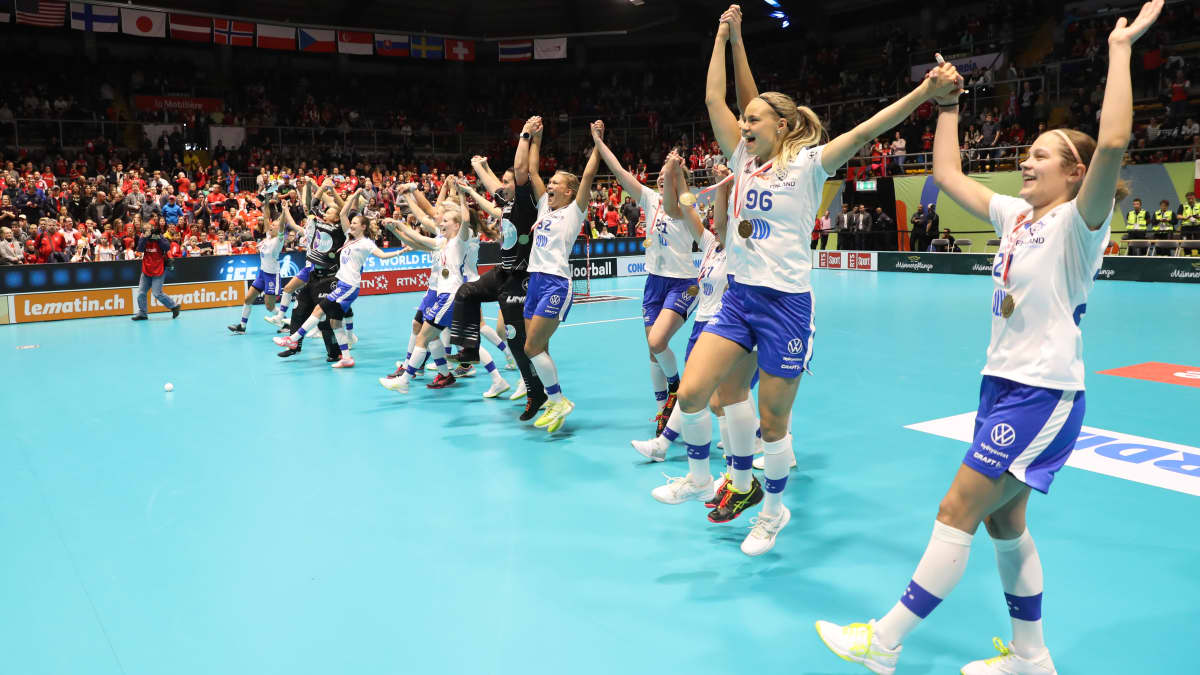 Suomen naisten salibandymaajoukkue tuulettaa pronssimitalia kädet ylhäällä rivissä.