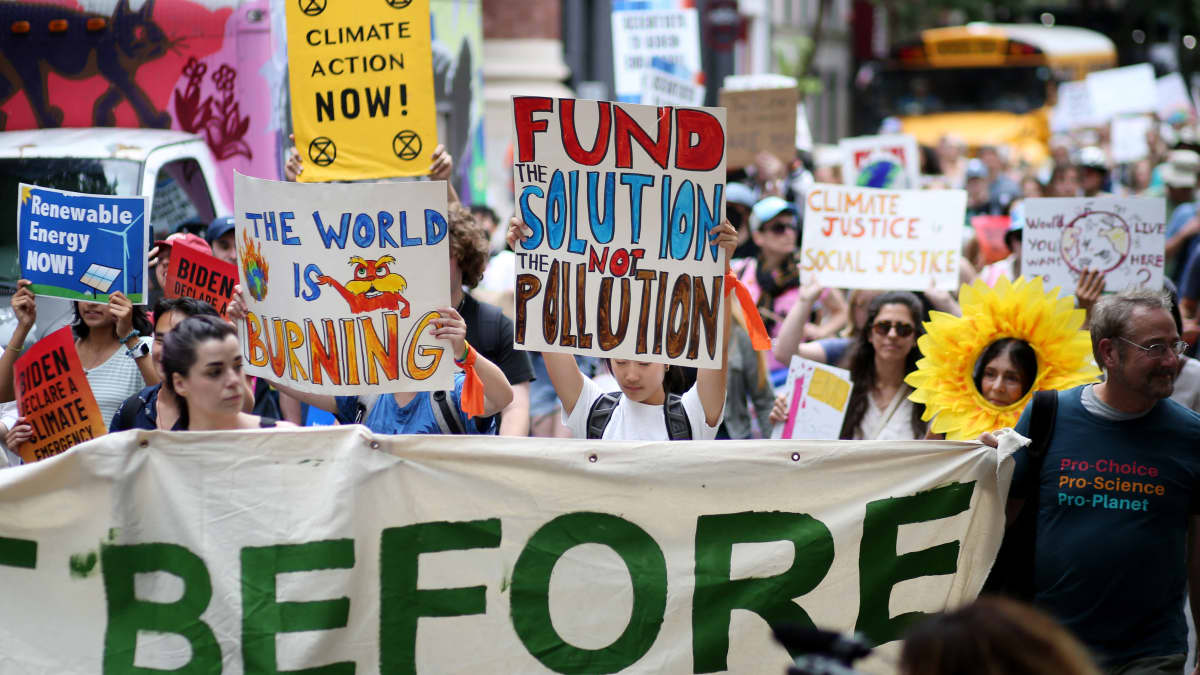 Mielenosoittajat kantavat kulkueessa ilmastonmuutoksesta ja fossiilisista polttoaineista varoittavia kylttejä.