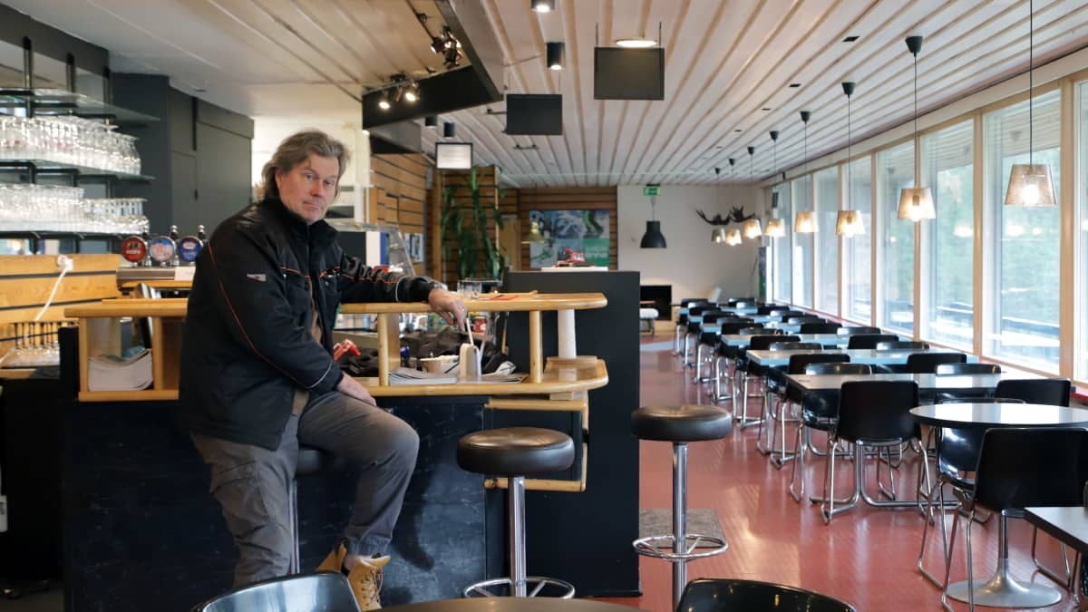 Kalpalinnan toimitusjohtaja Petri Ilmarinen istuu ravintolan baaritiskillä katse kameraan, oikealla pöytiä jonossa isojen ikkunoiden edessä.
