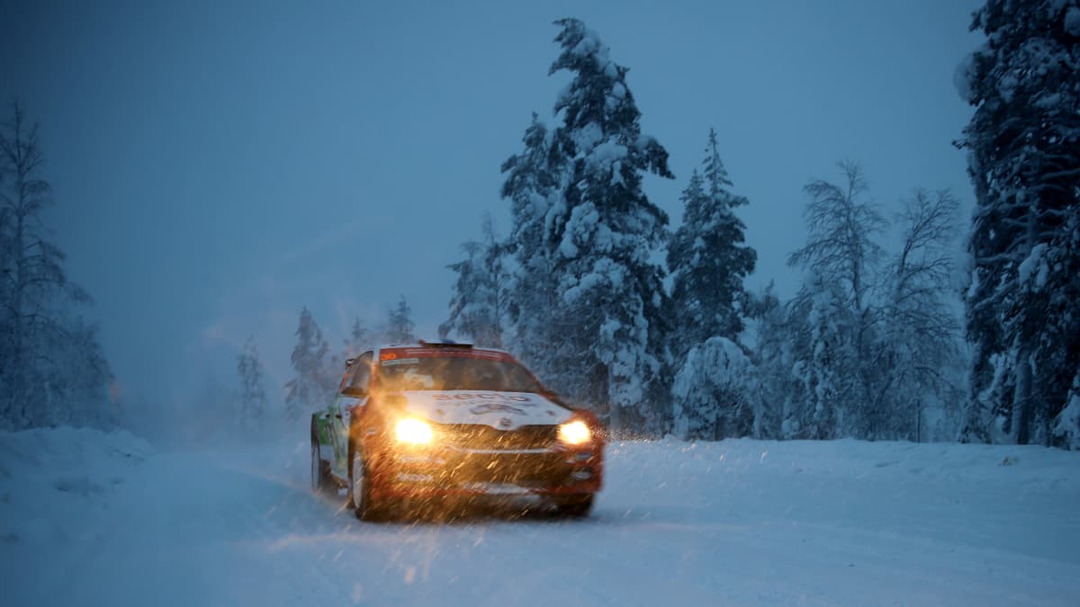 Ralliauto pimenevällä tiellä lumisateessa.