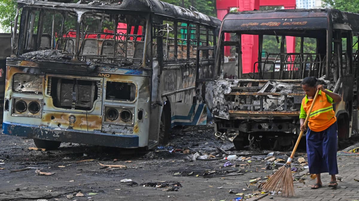 Nainen lakaisee katua kahden tuhoutuneen bussin edessä Sri lankan pääkaupungissa Colombossa