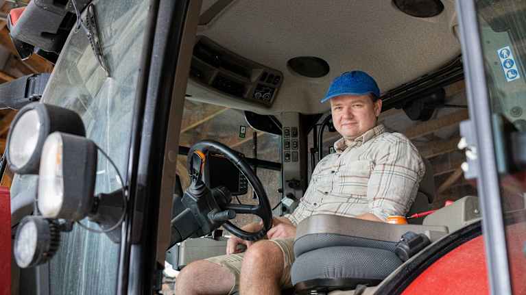En ung man som sitter i en traktor och ler mot kameran.