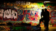 Två personer i står vid en graffitimålad vägg.