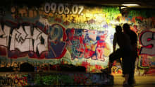 Två personer i står vid en graffitimålad vägg.