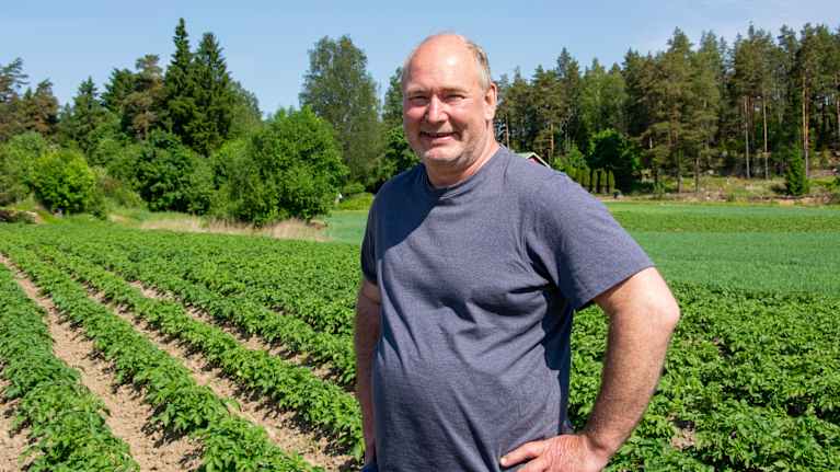 En man i t-shirt står på en åker och tittar in i kameran.