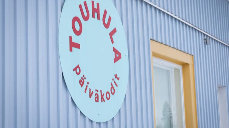 pyöreä Touhula päiväkodit -tunnus⁣ sinisen rakennuksen seinässä.