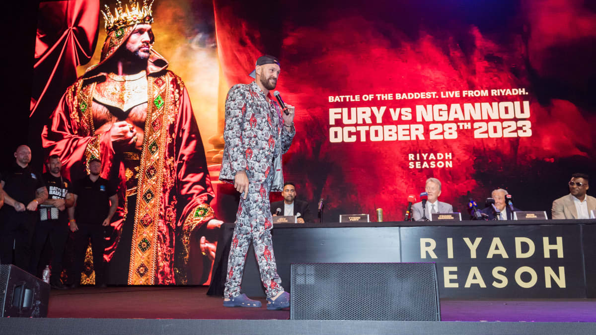 Tyson Fury puhuu mikrofoniin lavalla, jossa markkinoidaan nyrkkeilyottelua.