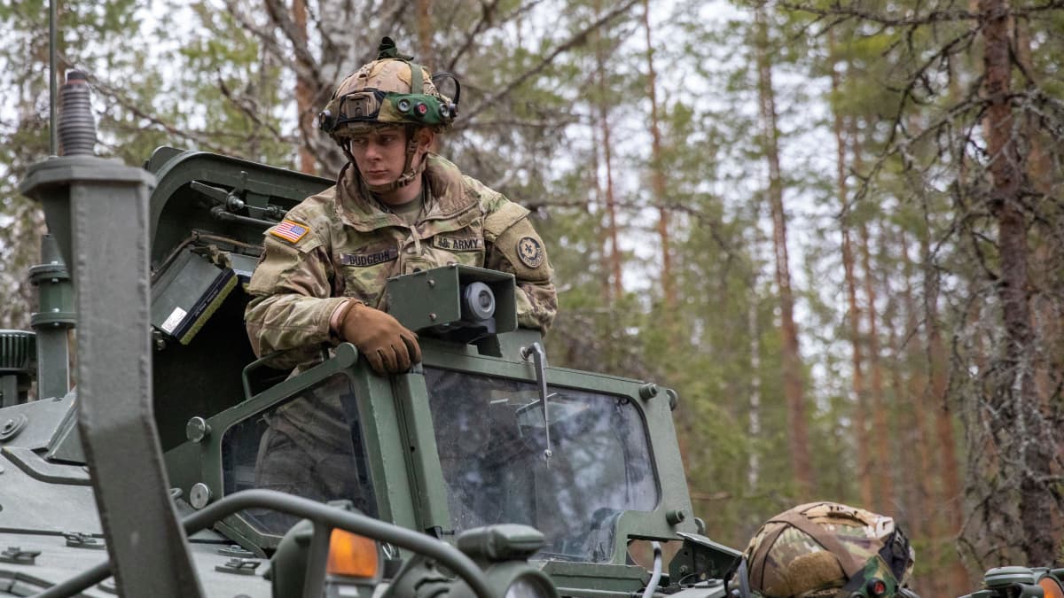 US soldier standing on a tank in the woods.
