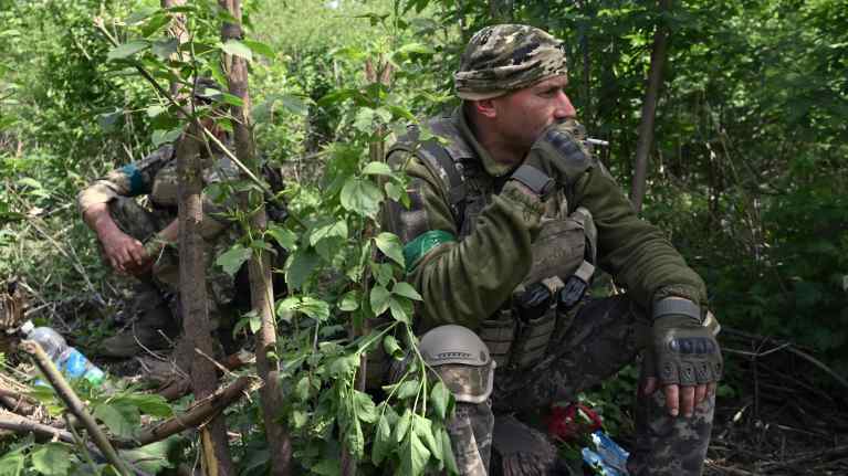 Sotilas polttaa tupakkaa oksien suojassa Ukrainassa.