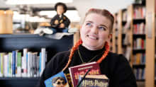 Nainen seisoo kirjastossa kädet täynnä Harry Potter -kirjoja.