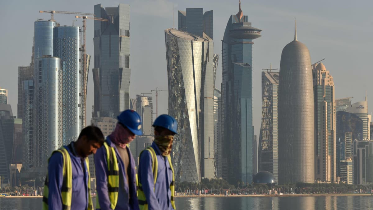 Rakennustyöntekijöitä kävelemässä Dohan pilvenpiirtäjät taustalla.