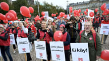 Demonstranter med röda västar och ballonger står på Järnvägstorget med Ateneum i bakgrunden. På skyltarna som demontranterna bär finns vårdarfacket Tehys logotyp och texter som "Lakko-oikeus - perusoikeus" (Strejkrätt - en grundläggande rätt).