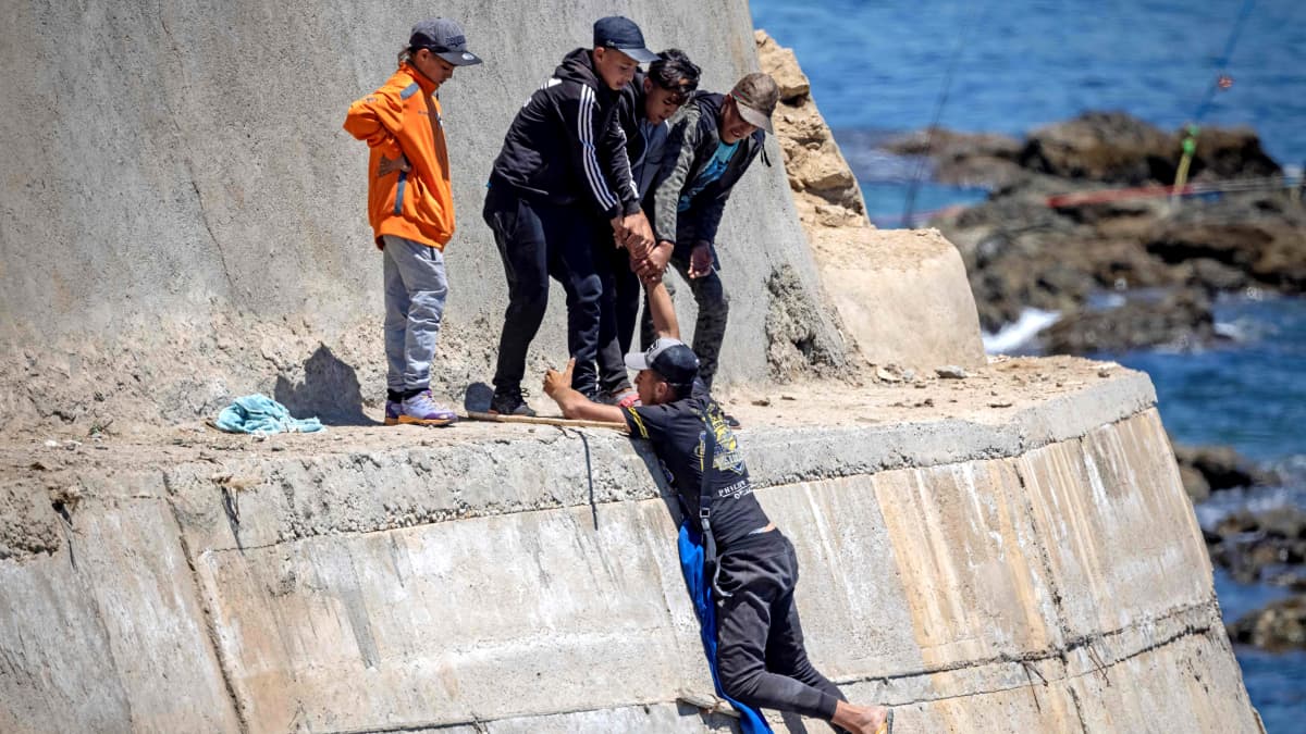 Eurooppaan pyrkivät siirtolaiset kiipeävät rannassa sijaitsevalle muurille.