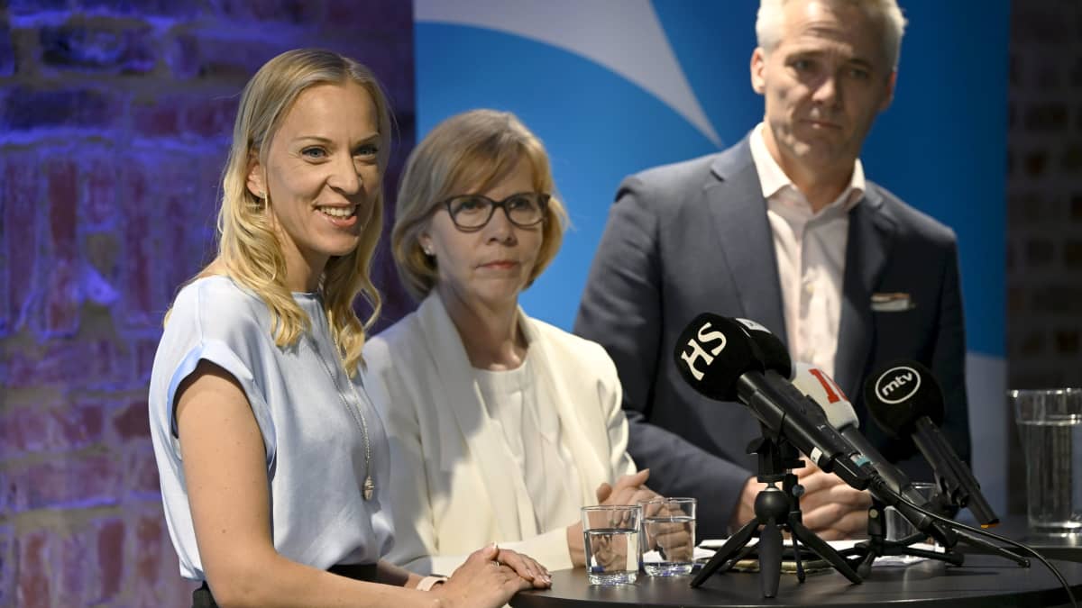Swedish Peoples Party ministerial nominees (from left) Sandra Bergqvist, Anna-Maja Henriksson and Anders Adlercreutz at a standing table with microphones on it.