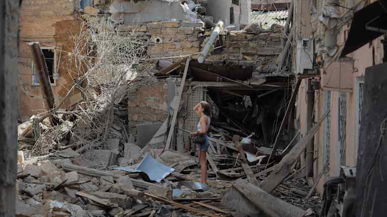 Woman standing in the ruins of a destroyed building.