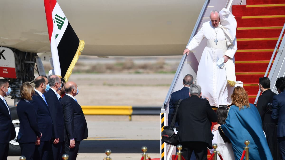 Paavi kävelee lentokoneen portaita alas, kaapu lepattaa.