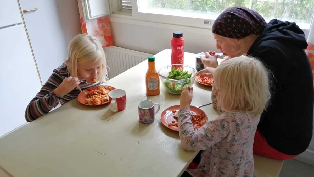 Holopaisen perhe syömässä vegaanilasagnea pöydän ääressä.