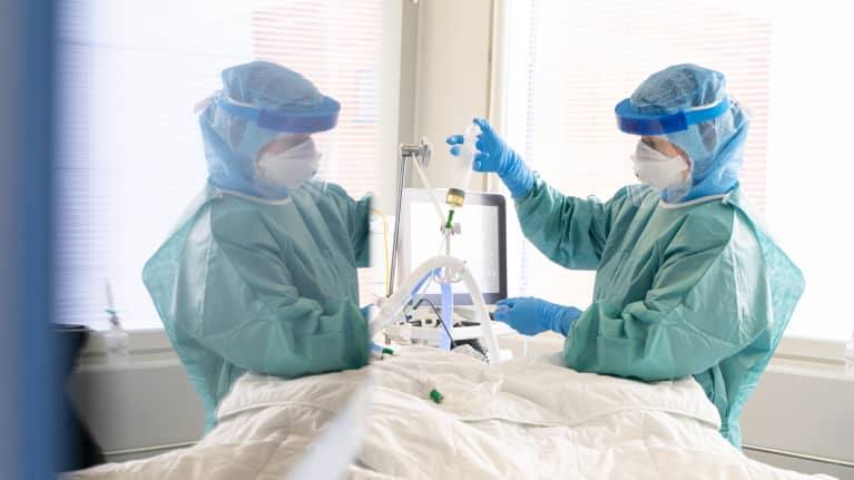 Lääkäri suojapuvussa hoitaa potilasta.