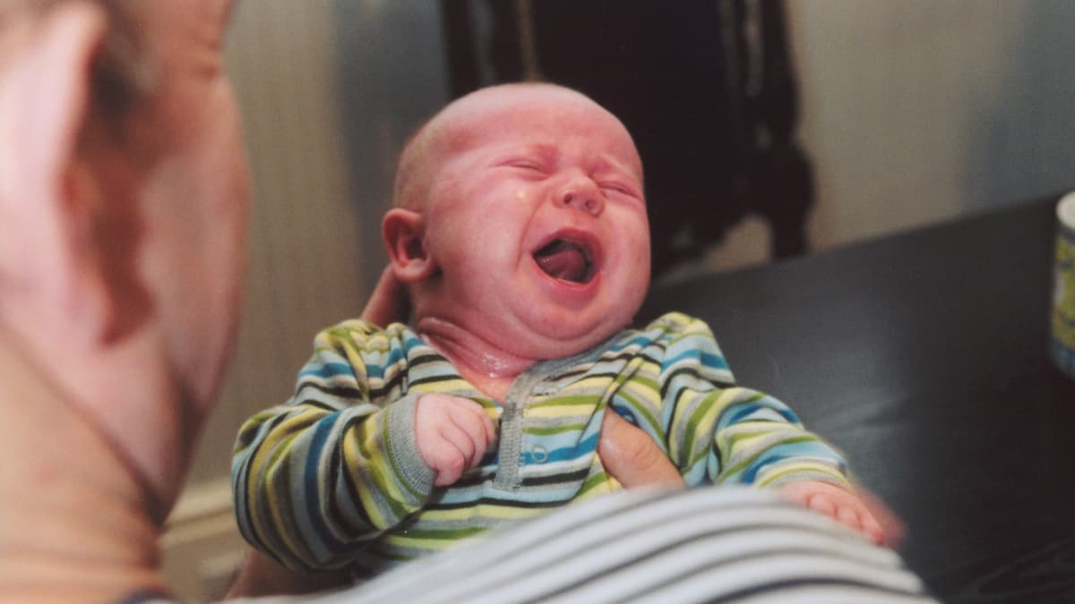 En pappa håller en fyramånaders baby som gråter.