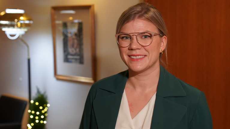 Riina Hiltunen, erikoistutkija, KELA, seisoo KELA:n käytävällä kameraan hymyillen.