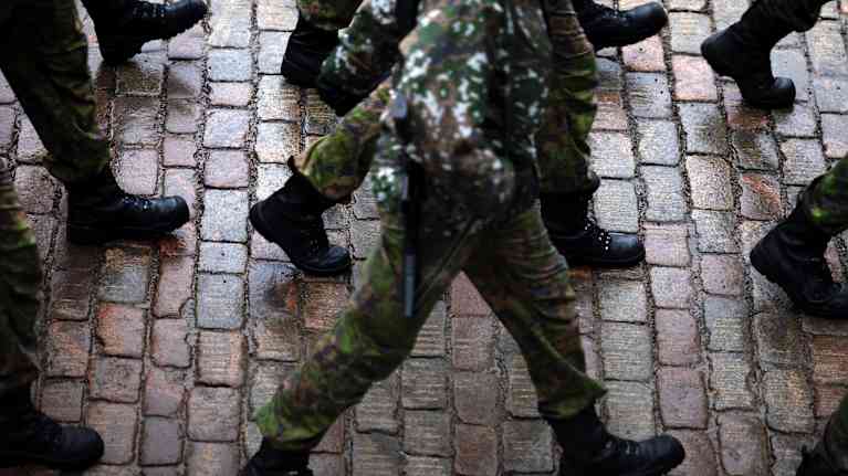 Around nine soldiers in military gear marching on a cobblestone street.