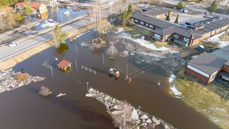Ilmakuva, jossa näkyy miten vesi on noussut puistoon Alavieskassa, puiston laidalla on kunnantalo vain muutaman metrin päässä vedestä.