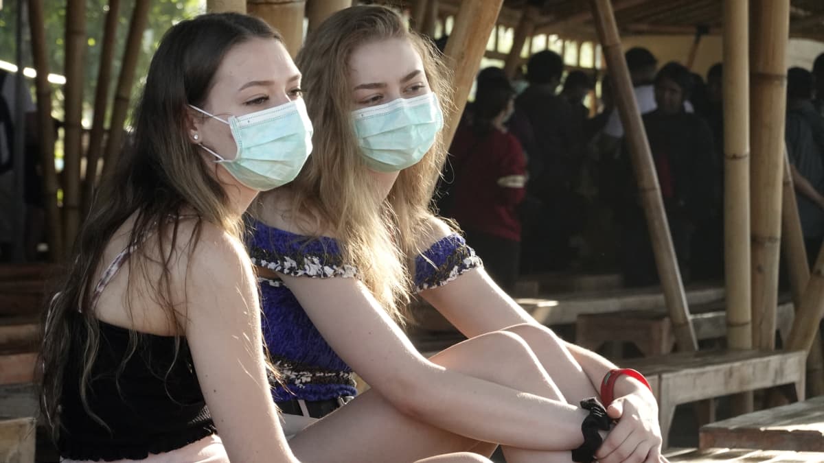Kaksi nuorta naista istuu rannalla kasvoillaan hengityssuojaimet.