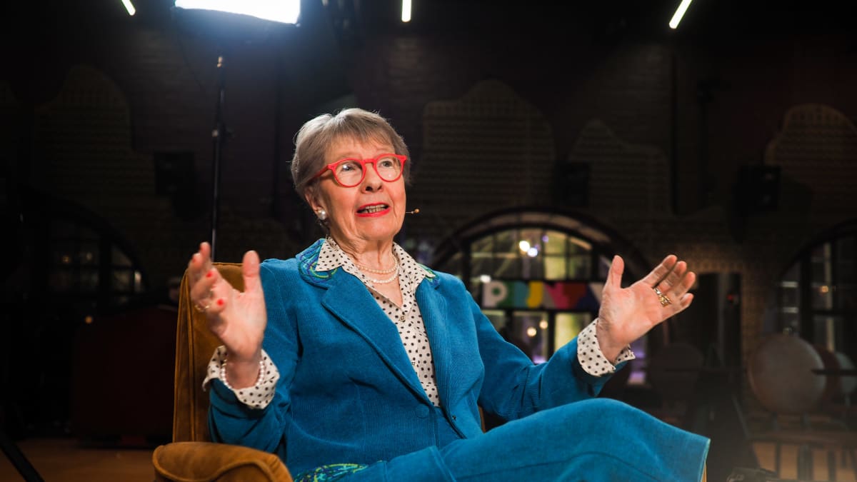 Sirkka-Liisa Kivelä istuu nojatuolissa ja levittelee käsiään.