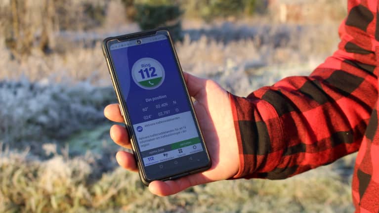 Hand håller fram telefon med 112 appen.