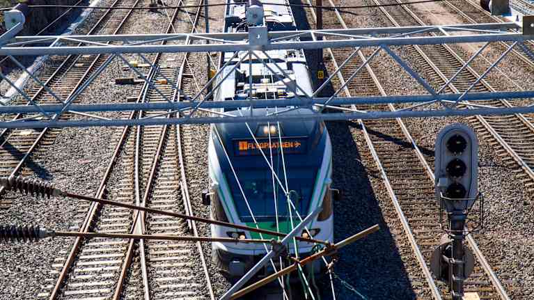 Commuter train and several train tracks alongside it seen from above, with metal frames and wires in the foreground.