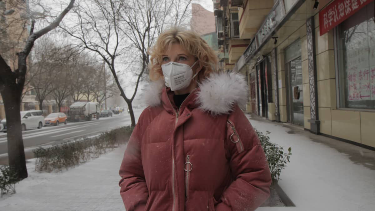 Ulla Nurmenniemi seisoo lumisella kadulla toppatakki päällä ja hengityksensuojain kasvoillaan.