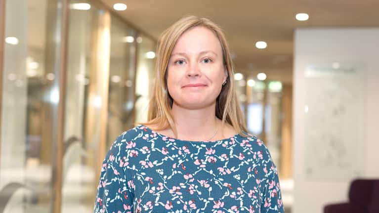 Vaaleahiuksinen nainen katsoo hymyillen kameraan.