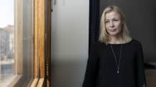 Tumma-asuinen nainen katsoo ulos ikkunasta.
