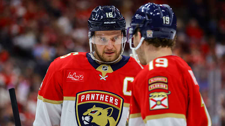 Två spelare snackar med varandra på isen.