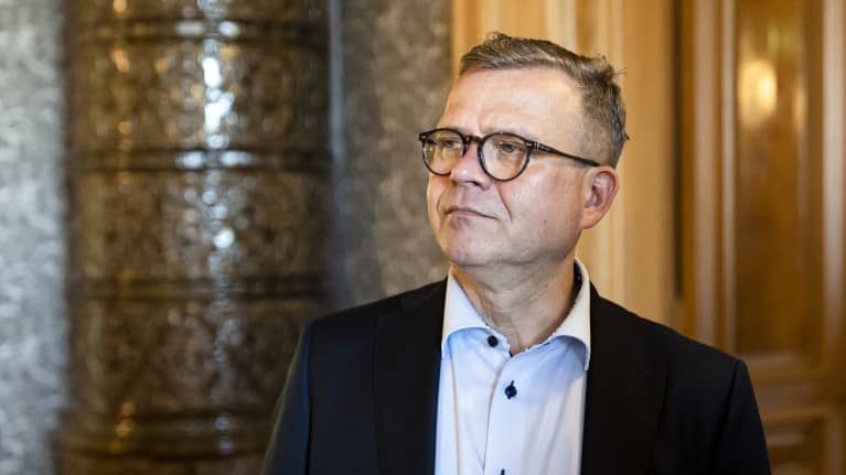 Petteri Orpo katsoo sivulle. Hänellä on silmälasit ja puku.