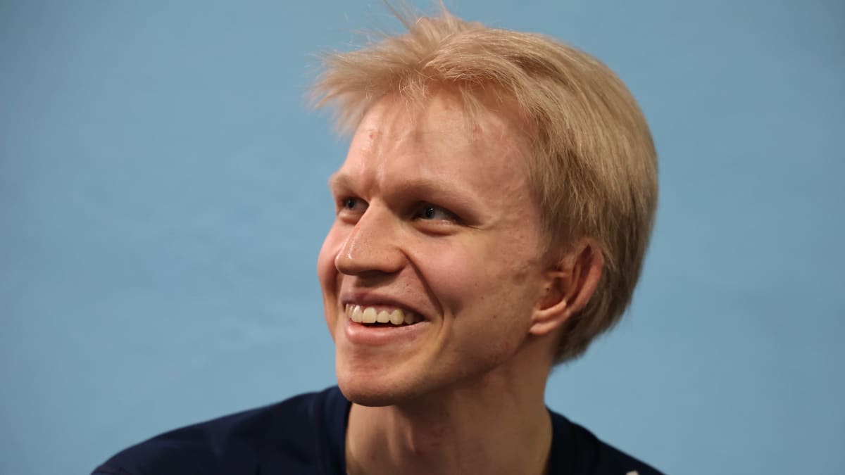 Nuori, vaaleahiuksinen mies katsoo vasemmalle ja hymyilee. Miehellä on päällään urheilulliset vaatteet.