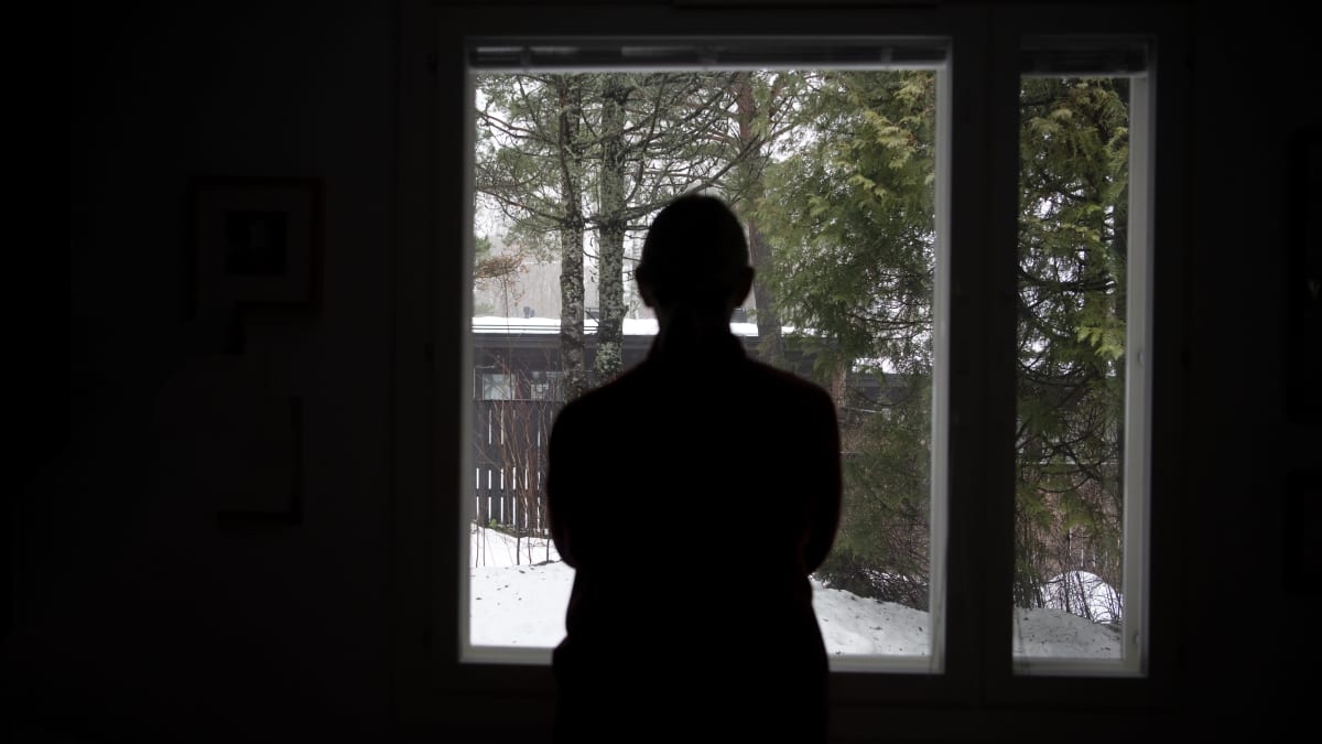 Photo shows the silhouette of a person standing in front of a window.